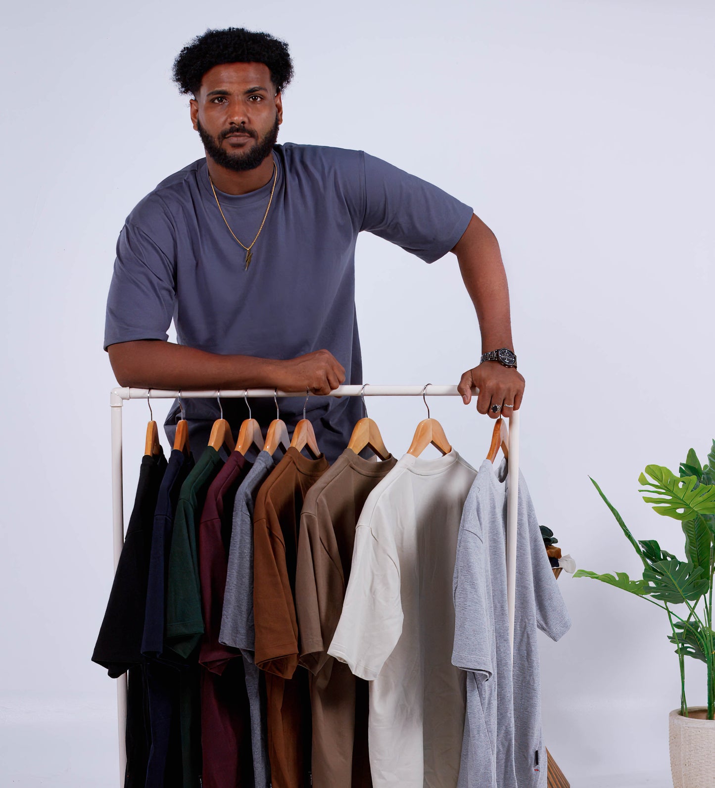 A person standing next to a rack of various colored clothing items on hangers, with the clothing item in focus being a medium gray shirt.